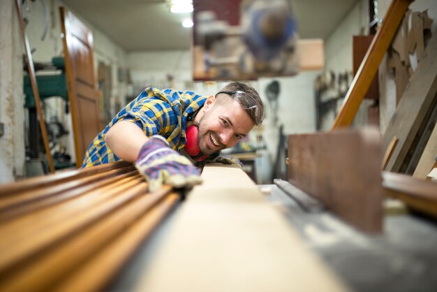 Retrato de trabajador carpintero experimentado cortando tablones de madera en la máquina en su taller de carpintería