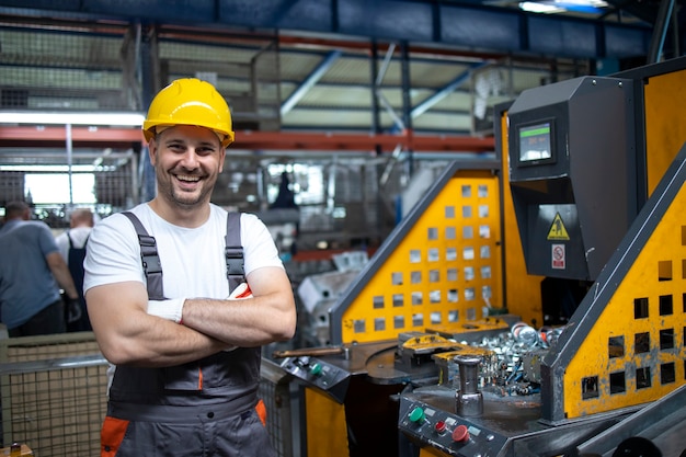 Foto gratuita retrato de trabajador de fábrica con los brazos cruzados de pie junto a la máquina industrial en la planta de producción