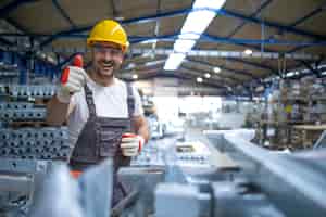 Foto gratuita retrato de trabajador de fábrica en equipo de protección sosteniendo thumbs up en la sala de producción