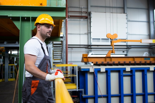 Retrato de trabajador de fábrica masculino apoyado en barandas de metal en la sala de producción industrial