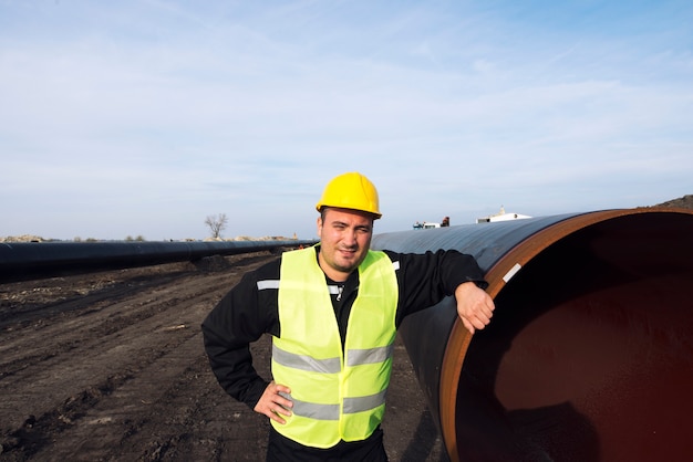 Retrato de un trabajador industrial de pie junto a la tubería de gas en el sitio de construcción