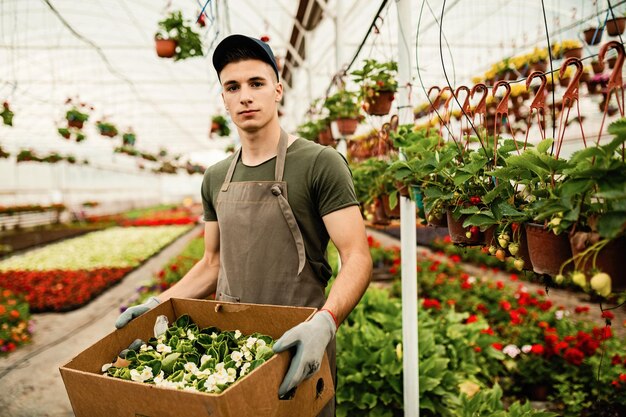 Retrato de un trabajador de invernadero que lleva una caja de flores preparada para la distribución