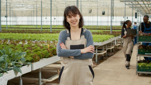 Retrato de un trabajador de invernadero que trabaja en un invernadero mientras los ingenieros agrícolas usan una laptop para ver el estado de entrega. Mujer caucásica en ambiente hidropónico con cajas de ensalada.