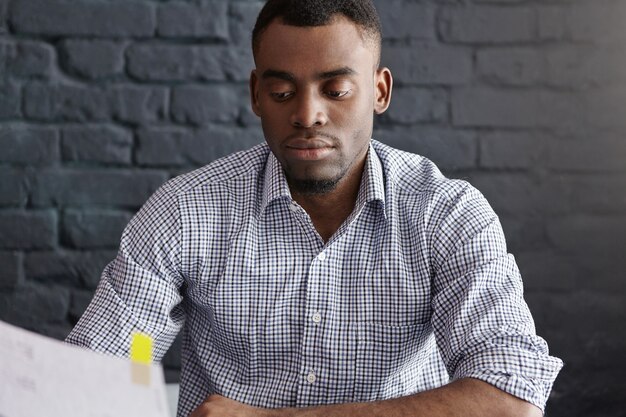 Retrato de trabajador de oficina afroamericano atractivo seguro analizando papeles durante el almuerzo en el restaurante