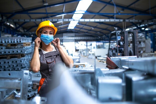 Retrato de trabajadora de fábrica en uniforme y casco con máscara facial en la planta de producción industrial