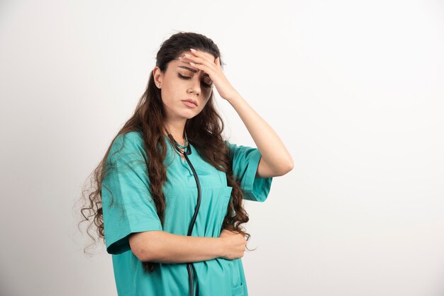 Retrato de trabajadora sanitaria tocando su cabeza en la pared blanca.