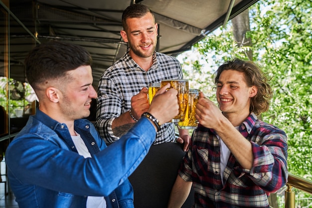 Retrato de tres amigos varones bebiendo cerveza en el pub.