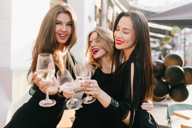 Retrato de tres hermanas en traje negro celebrando un evento importante con champán