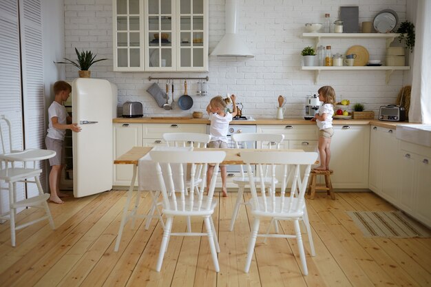 Retrato de tres hermanos niños independientes preparando la cena ellos mismos mientras los padres en el trabajo. Niños preparando el desayuno juntos en la cocina. Concepto de alimentación, culinaria, cocina, infancia y nutrición.