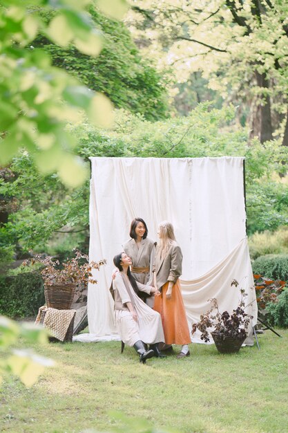 Retrato de tres hermosas mujeres en el jardín, de pie, sentado y sonriendo durante el día.