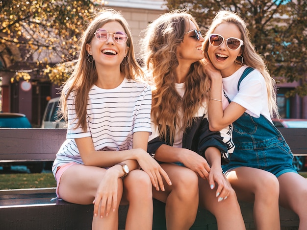 Retrato de tres jóvenes hermosas chicas hipster sonrientes en ropa de moda de verano. Mujeres despreocupadas sexy posando en la calle. Modelos positivos divirtiéndose en gafas de sol.