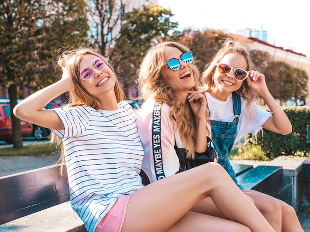 Retrato de tres jóvenes hermosas chicas hipster sonrientes en ropa de moda de verano. Mujeres despreocupadas sexy posando en la calle. Modelos positivos divirtiéndose en gafas de sol.