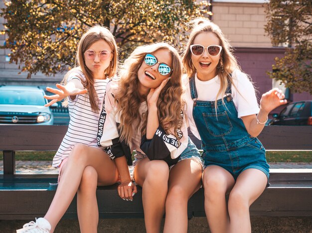 Retrato de tres jóvenes hermosas chicas hipster sonrientes en ropa de moda de verano. Mujeres despreocupadas sexy posando en la calle. Modelos positivos divirtiéndose en gafas de sol.