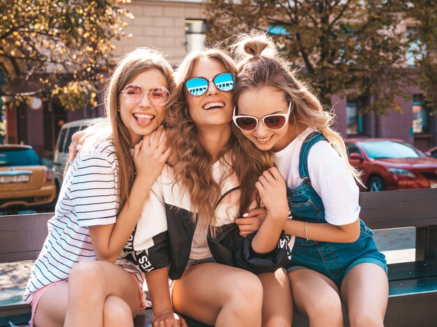 Retrato de tres jóvenes hermosas chicas hipster sonrientes en ropa de moda de verano. Mujeres despreocupadas sexy posando en la calle. Modelos positivos divirtiéndose en gafas de sol.