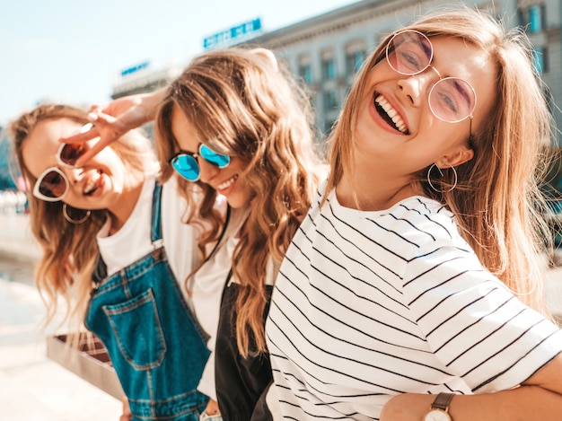 Retrato de tres jóvenes hermosas chicas hipster sonrientes en ropa de moda de verano. Mujeres despreocupadas sexy posando en la calle. Modelos positivos divirtiéndose en gafas de sol.