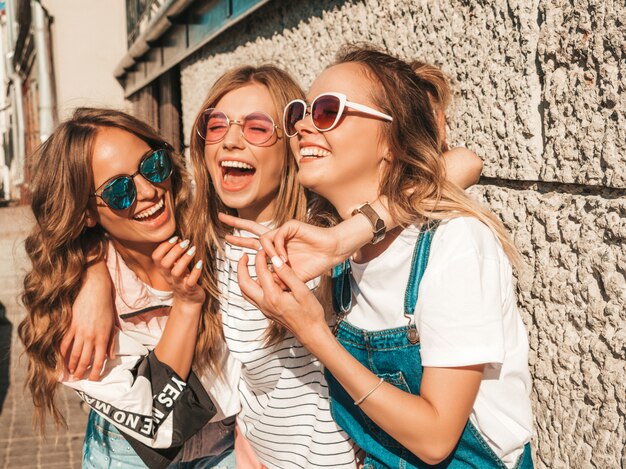 Retrato de tres jóvenes hermosas chicas hipster sonrientes en ropa de moda de verano. Mujeres despreocupadas sexy posando en la calle. Modelos positivos divirtiéndose en gafas de sol.