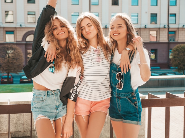 Retrato de tres jóvenes hermosas chicas hipster sonrientes en ropa de moda de verano. Mujeres despreocupadas y sexy posando en la calle. Modelos positivos divirtiéndose. Levantan las manos