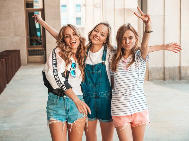 Retrato de tres jóvenes hermosas chicas hipster sonrientes en ropa de moda de verano. Mujeres despreocupadas y sexy posando en la calle. Modelos positivos divirtiéndose. Levantan las manos