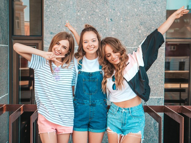 Retrato de tres jóvenes hermosas chicas hipster sonrientes en ropa de moda de verano. Mujeres despreocupadas y sexy posando en la calle. Modelos positivos divirtiéndose. Levantan las manos