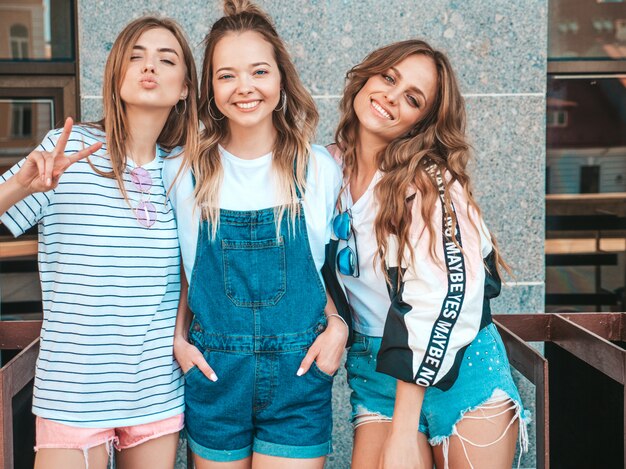 Retrato de tres jóvenes hermosas chicas hipster sonrientes en ropa de moda de verano. Mujeres despreocupadas y sexy posando en la calle. Modelos positivos divirtiéndose.