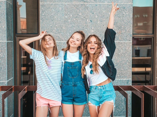 Retrato de tres jóvenes hermosas chicas hipster sonrientes en ropa de moda de verano. Mujeres despreocupadas y sexy posando en la calle. Modelos positivos divirtiéndose.