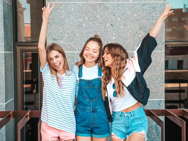 Retrato de tres jóvenes hermosas chicas hipster sonrientes en ropa de moda de verano. Sexy mujer despreocupada posando en la calle. Modelos positivos divirtiéndose. Levantando las manos