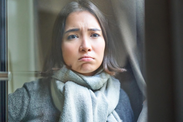 Retrato de una triste mujer enferma que se queda en casa mirando por la ventana con cara celosa y molesta