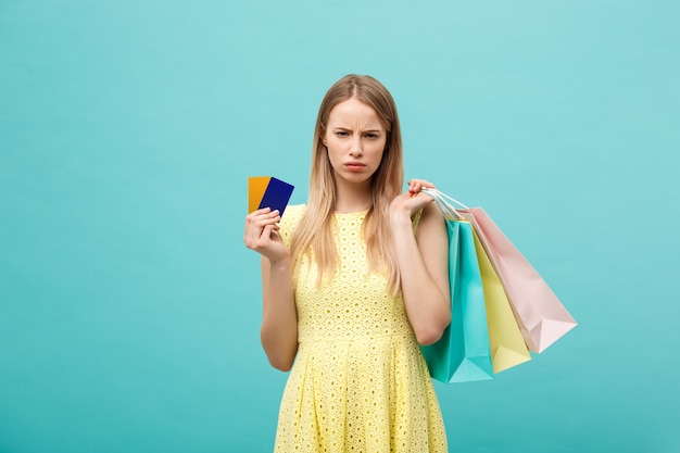 Retrato, de, un, triste, mujer, tenencia, bolsas de compras, y, tarjeta bancaria, aislado, en, un, fondo azul
