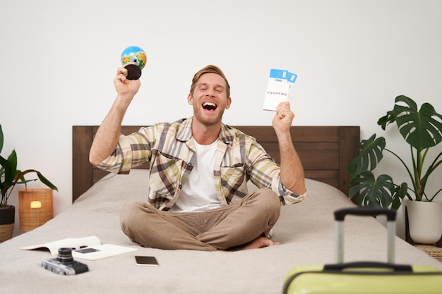 Retrato de un turista alegre y feliz sentado con boletos de avión y una maleta llena de globos para