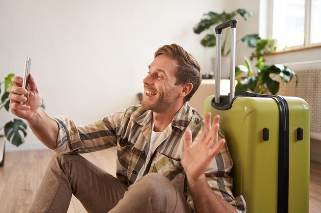 Retrato de un turista feliz tomando selfies antes de su vuelo con fotos en la maleta usando su teléfono inteligente