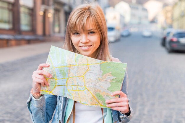 Retrato de un turista femenino sonriente que se coloca en la calle que muestra el mapa