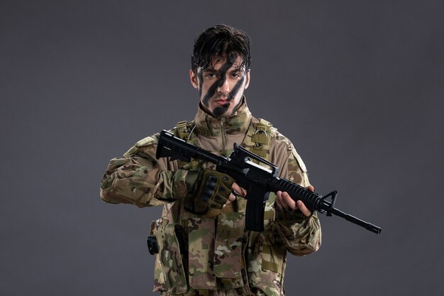 Retrato de valiente soldado en uniforme militar con ametralladora en la pared oscura