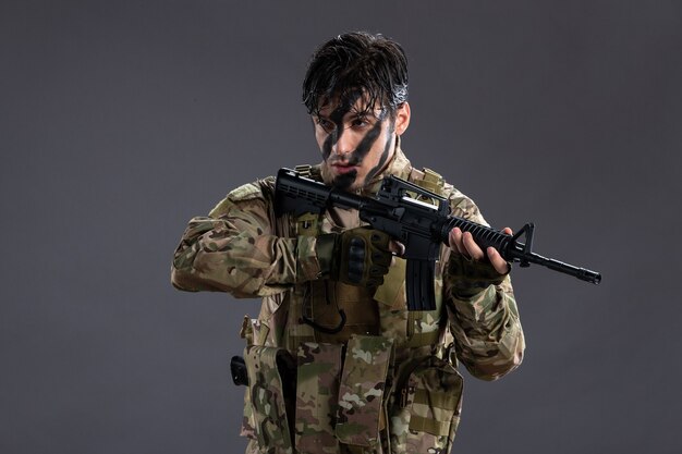 Retrato de valiente soldado en uniforme militar con ametralladora en la pared oscura