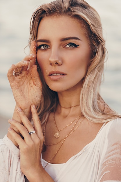 Retrato de verano al aire libre de hermosa mujer rubia feliz relajarse en la playa cerca del océano