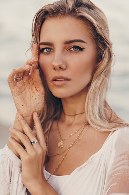 Retrato de verano al aire libre de hermosa mujer rubia feliz relajarse en la playa cerca del océano