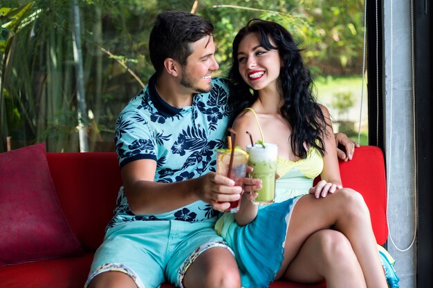 Retrato de verano de estilo de vida de un joven y una mujer disfrutan de su cita romántica, posando en un elegante café, bebiendo cócteles