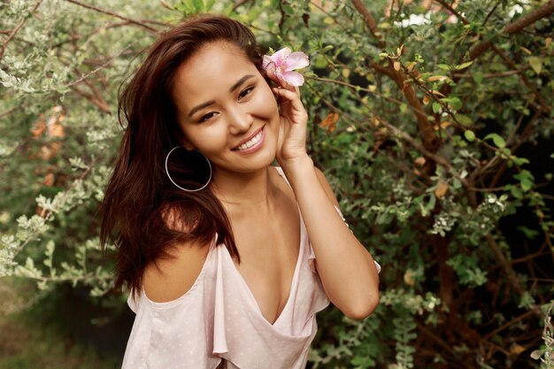 Retrato de verano de hermosa mujer asiática con flor en pelos posando en el jardín.