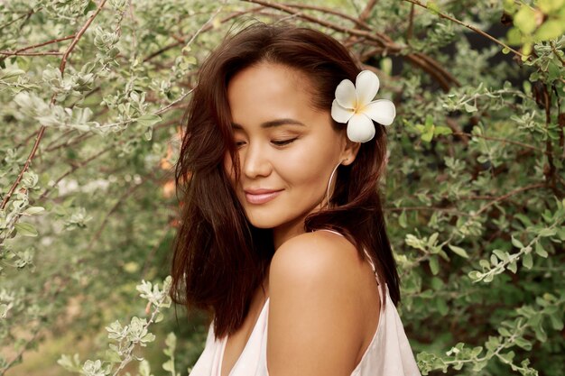 Retrato de verano de hermosa mujer asiática con flor en pelos posando en el jardín.