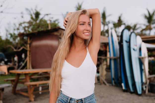 Retrato de verano de hermosa mujer joven vestida con camisa blanca con los hombros desnudos levantando las manos y mirando a un lado