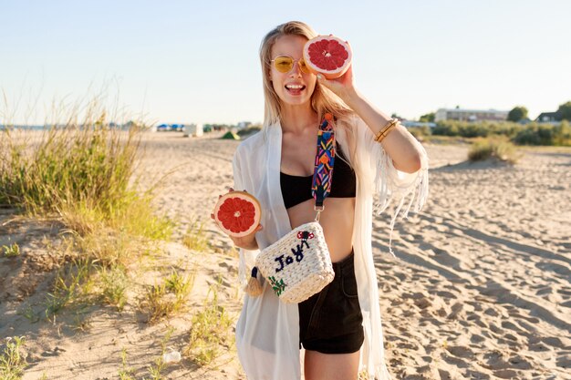 Retrato de verano de mujer despreocupada juguetona posando con mitades de pomelo sabroso en las manos.