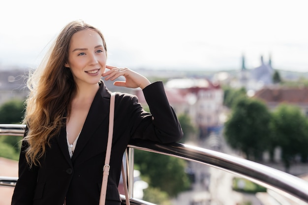 Retrato de verano de mujer joven relajante en la terraza de la azotea sobre fondo de vista de la ciudad europea.