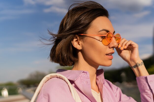 Retrato de verano de mujer de pelo muy corto con elegantes gafas de sol caminando al aire libre