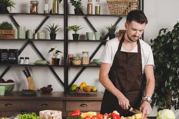 Retrato de verduras corte joven con un cuchillo en la cocina