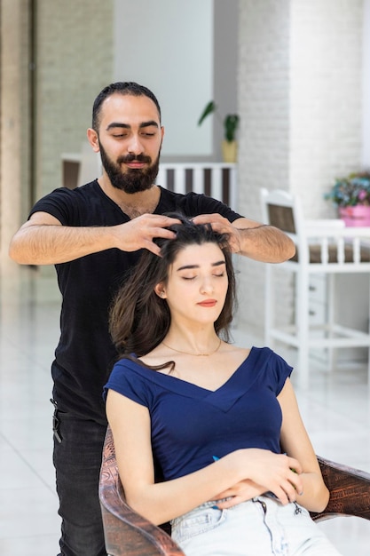 Retrato vertical de un joven barbero haciendo un masaje en la cabeza a su cliente Foto de alta calidad