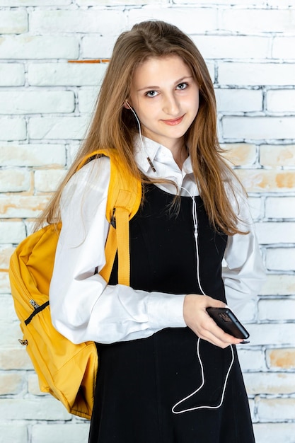 Retrato vertical de una joven colegiala usando auriculares y mirando la cámara