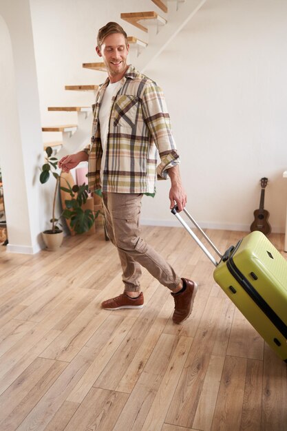 Foto gratuita retrato vertical de un joven feliz con una maleta caminando en el interior dejando un apartamento con equipaje yendo