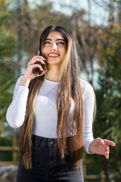 Retrato vertical de una joven hermosa hablando por teléfono en el parque Foto de alta calidad