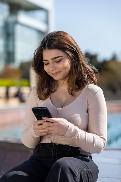 Retrato vertical de una joven hermosa mirando su teléfono y sonriendo Foto de alta calidad