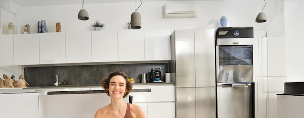 Foto gratuita retrato vertical de una joven instructora de fitness y entrenadora de atención plena sentada en el suelo de su casa en