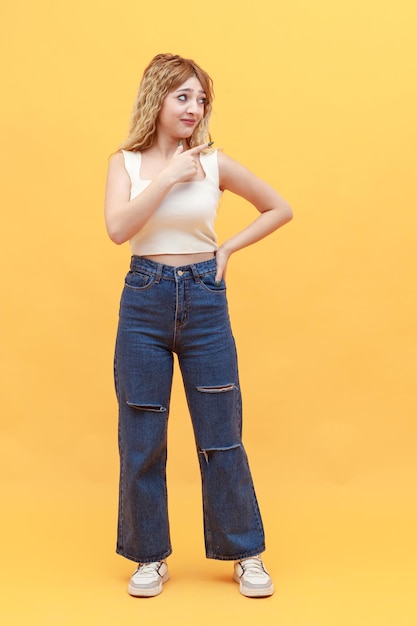 Retrato vertical de una joven rubia señalando con el dedo a un lado sobre fondo amarillo